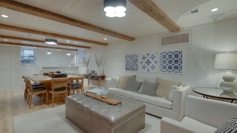 Inviting living area with a cream sofa, a tufted ottoman, and blue tile artwork under wooden beams.