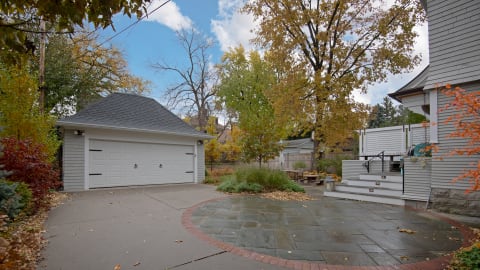 A modern property with a garage, stone patio, and outdoor seating area surrounded by autumn trees.