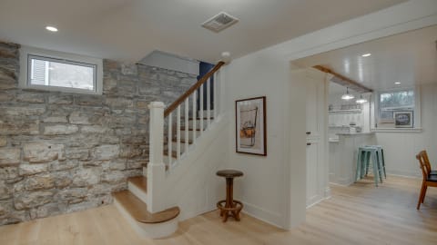 Open living area with exposed stone walls, hardwood floors, and a staircase leading upwards.