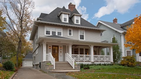 A classic two-story home with a porch, surrounded by autumn foliage.
