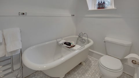 A sophisticated bathroom featuring a white clawfoot tub with a bathtub caddy, towels, and a modern toilet.