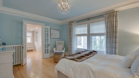 A tranquil bedroom featuring a crystal chandelier, white linens, and blue walls.