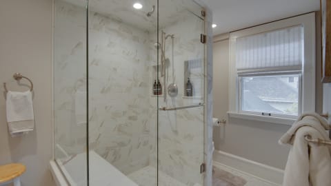 A luxurious bathroom with a glass-enclosed shower featuring marble-style tiles and elegant fixtures.