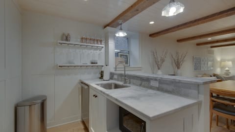 Stylish kitchen with marble countertops, wooden beams, glassware display, and cozy decor.