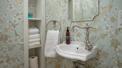 A powder room with floral wallpaper, a sink with a stylish faucet, soap dispenser, and fluffy towels on a shelf.