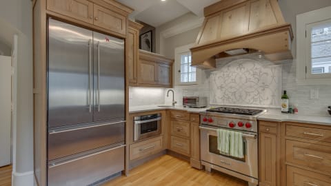 A gourmet kitchen with stainless steel appliances, wooden cabinets, and a marble backsplash.