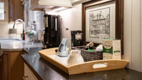 A cozy kitchen countertop with a wooden tray holding coffee, tea, and utensils, accompanied by a framed illustration.