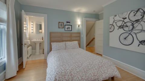 Cozy bedroom with blue walls, floral duvet, and artwork, leading to a bright bathroom.
