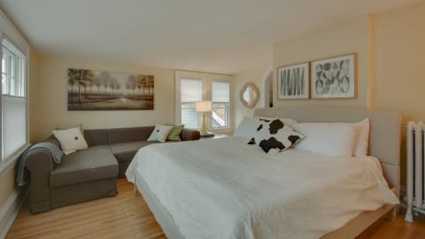 A cozy bedroom featuring a king-sized bed, a gray sectional sofa, and decorative artworks on the walls.