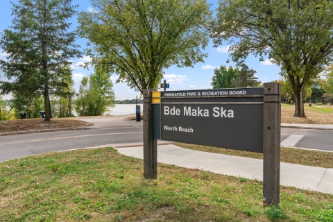 Sign indicating Bde Maka Ska North Beach with trees and the lake in the background.