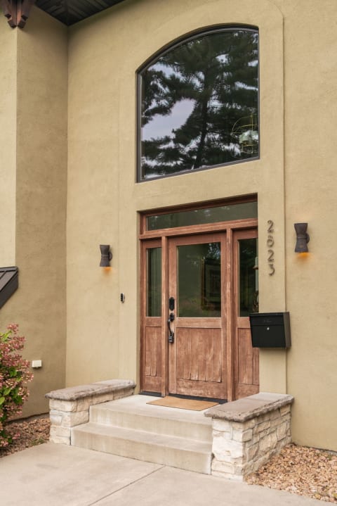 A welcoming entrance of a modern home with wooden doors and stone steps.