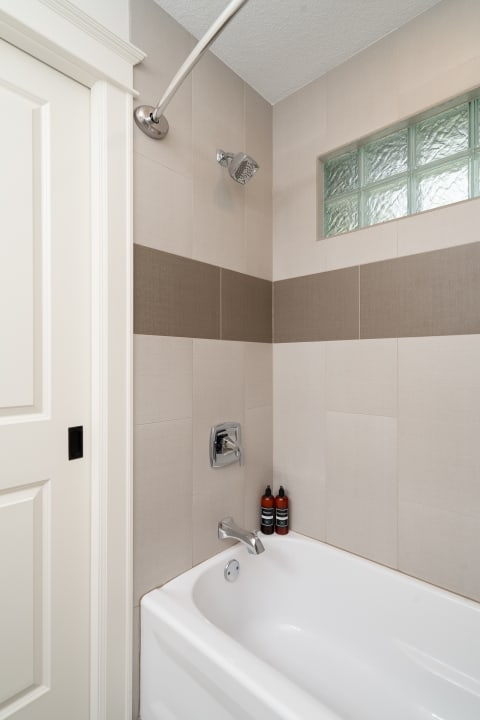 Modern bathroom with a white bathtub and stylish tiles, showcasing a showerhead and bath products.