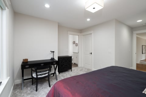 A stylish bedroom with a black desk, decorative cabinet, and a bed with purple and red bedding.