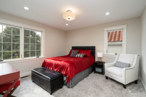 Modern bedroom with red bedding, black accents, and a reading chair.