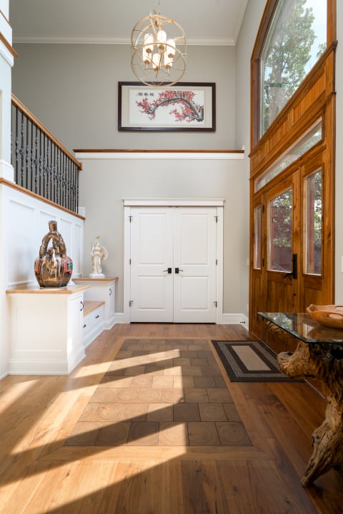 An elegant entryway with a chandelier, artwork, and wooden furnishings.