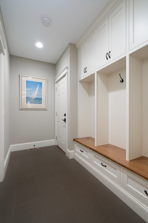A spacious mudroom featuring white cabinetry, a wooden bench, a large door, and maritime artwork.