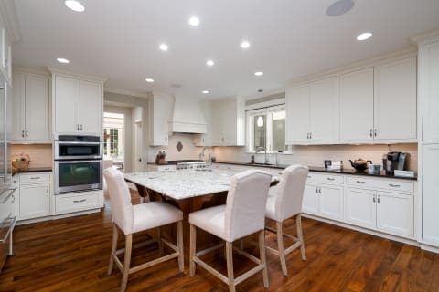 A spacious modern kitchen featuring white cabinets, granite counters, and hardwood floors.