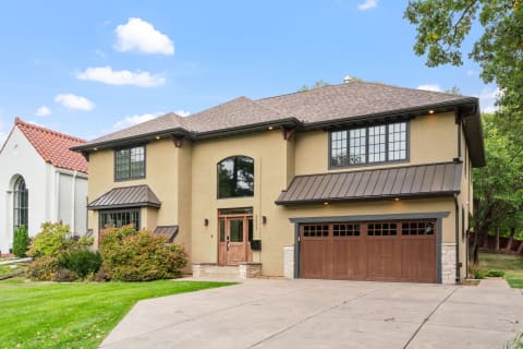 A modern house with a stucco exterior, large windows, and a two-car garage, surrounded by greenery.