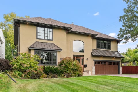 A stylish two-story house with beige exterior and dark brown accents, featuring a well-maintained lawn and landscaping.