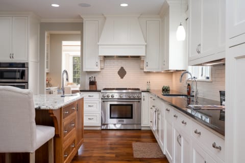 A bright and modern kitchen featuring white cabinets, dark granite counters, and a wood-finished island.