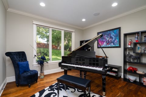 Elegant music room featuring a grand piano, a tufted blue chair, and decorative items.