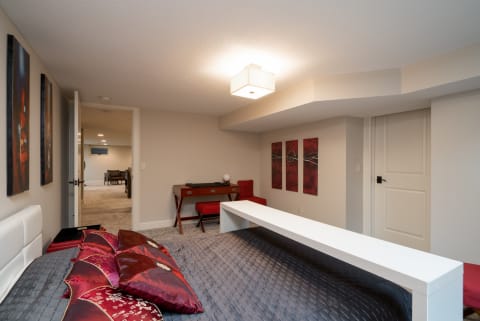 Cozy bedroom in a basement with decorative pillows, desk area, and warm lighting.