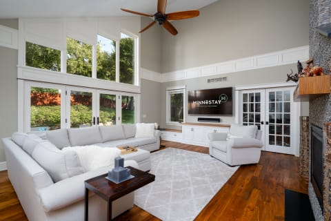 Living room with high ceilings, large windows, and modern furnishings including a gray sectional sofa and a wall-mounted TV.