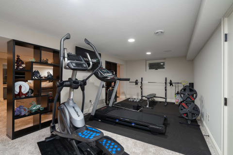 Home gym with elliptical machine, treadmill, weight bench, and decorative shelves.