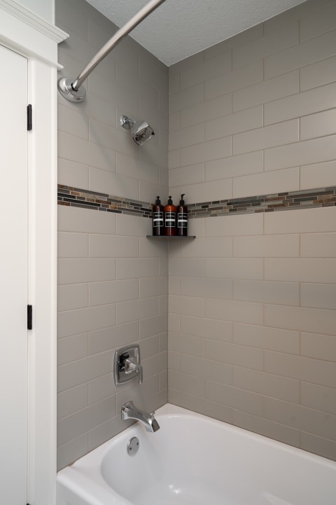 A modern bathroom featuring a light gray tiled shower area and a white soaking tub with chrome fixtures.