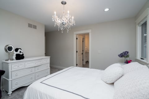 Cozy bedroom with a white bed, chandelier, and a panda stuffed animal on a dresser.