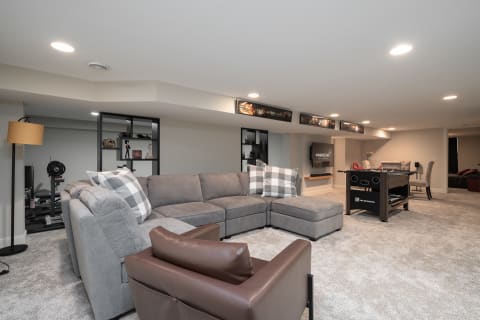 Modern basement living area with a sectional sofa, decorative pillows, and a foosball table.