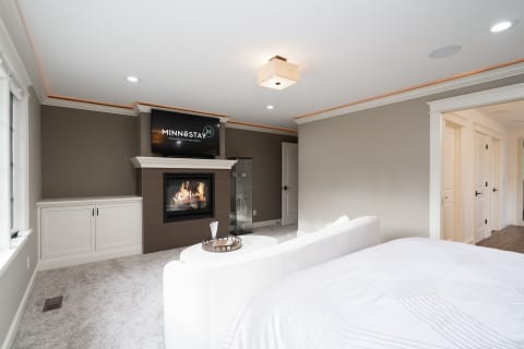 Interior of a contemporary master bedroom with a fireplace and modern furnishings.