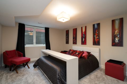 A cozy bedroom featuring a bed with rich pillows, a red armchair, and modern artwork on the walls.