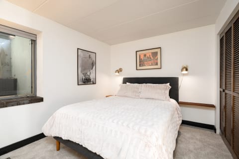 A modern bedroom featuring a queen-sized bed, art on the walls, and a window with natural light.