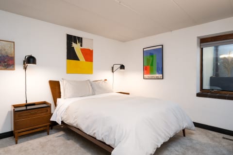 A neatly arranged bedroom with a bed, nightstand, and colorful wall art.