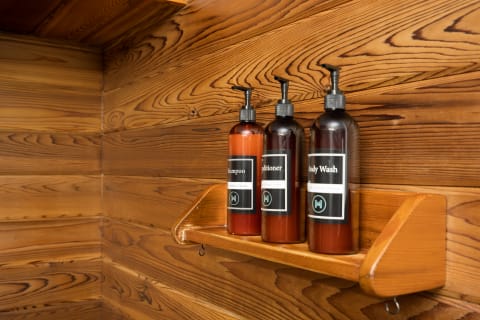 Three bottles of shampoo, conditioner, and body wash on a wooden shelf in a natural wood environment.