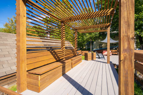A wooden pergola with horizontal slats and benches on a light deck.