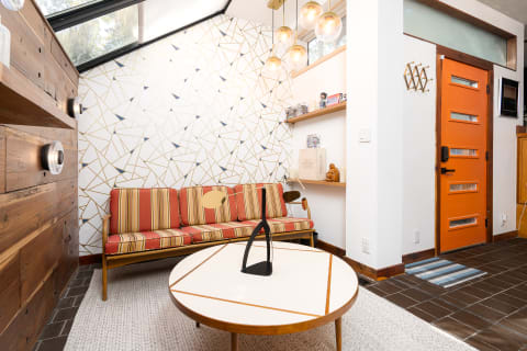 A stylish living room with a retro sofa, geometric wall design, and an orange front door.