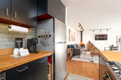 A modern kitchen with a coffee maker and a cozy living area featuring a gray couch and artistic decor.