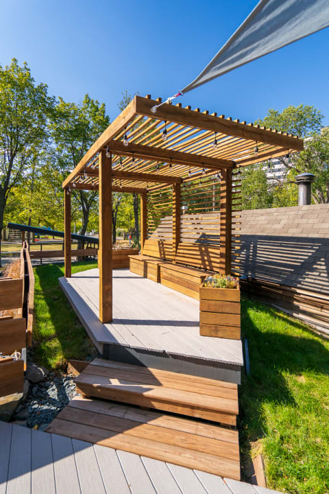 Modern wooden pergola with a slatted roof and spacious deck area surrounded by greenery.