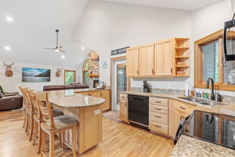 Interior view of a rustic lake house kitchen with wooden cabinets, granite countertops, and a living area.