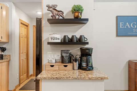 A cozy kitchen nook with a coffee maker, moose figurine, and gray mugs on display.