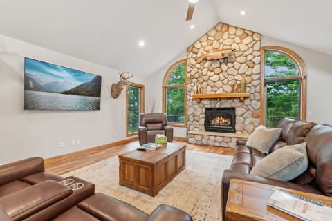 Cozy living room with stone fireplace, seating area, and natural views through large windows.