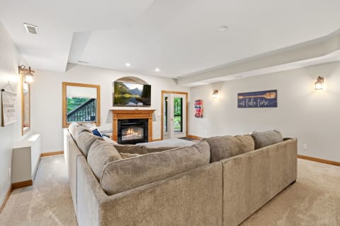 Spacious living room with a beige sofa, fireplace, and large TV displaying a landscape.