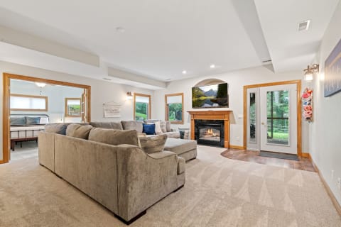 A well-lit living room with a sofa, fireplace, and a view of greenery outside.