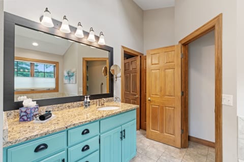 A modern bathroom featuring a turquoise cabinet vanity, granite countertop, and wooden doors.