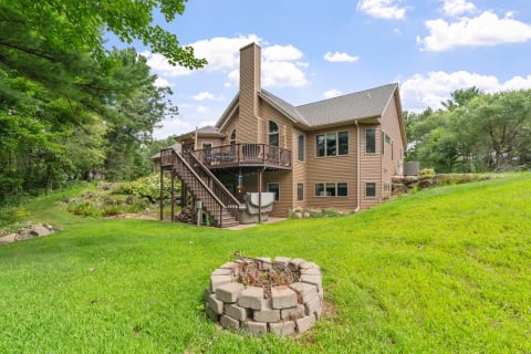 Back view of a modern two-story house with a wooden deck and lush lawn.