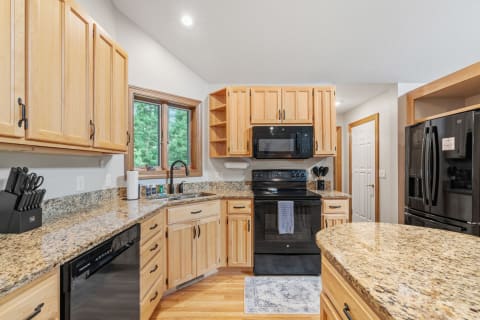 A modern kitchen featuring light wood cabinetry, dark appliances, and a window view of greenery.