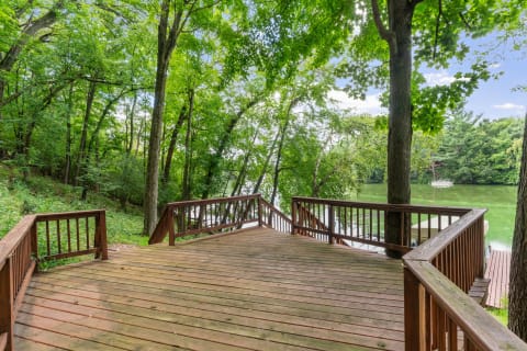 Wooden deck surrounded by trees with a view of a lake and a sailboat in the distance.