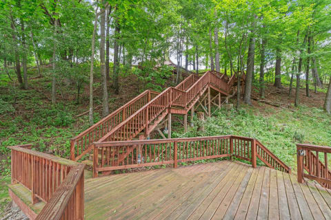 A wooden staircase ascends through a green forest with a wooden deck in foreground.